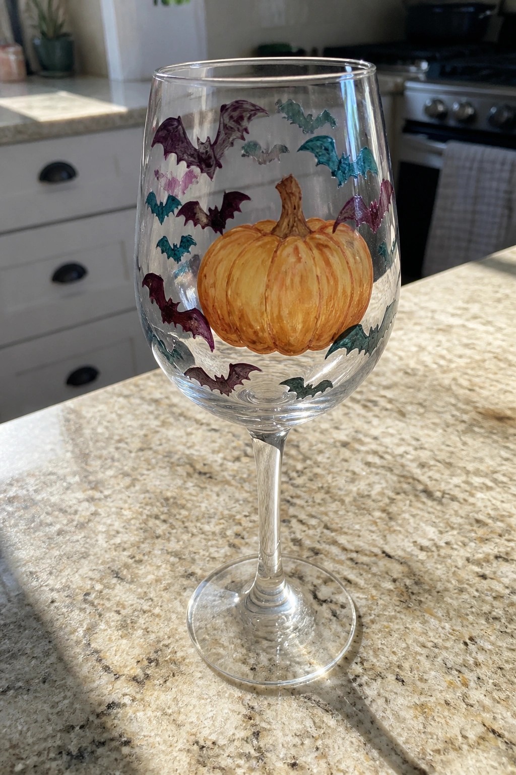 Stemmed wine glass with orange pumpkin and purple teal bat paintings on counter