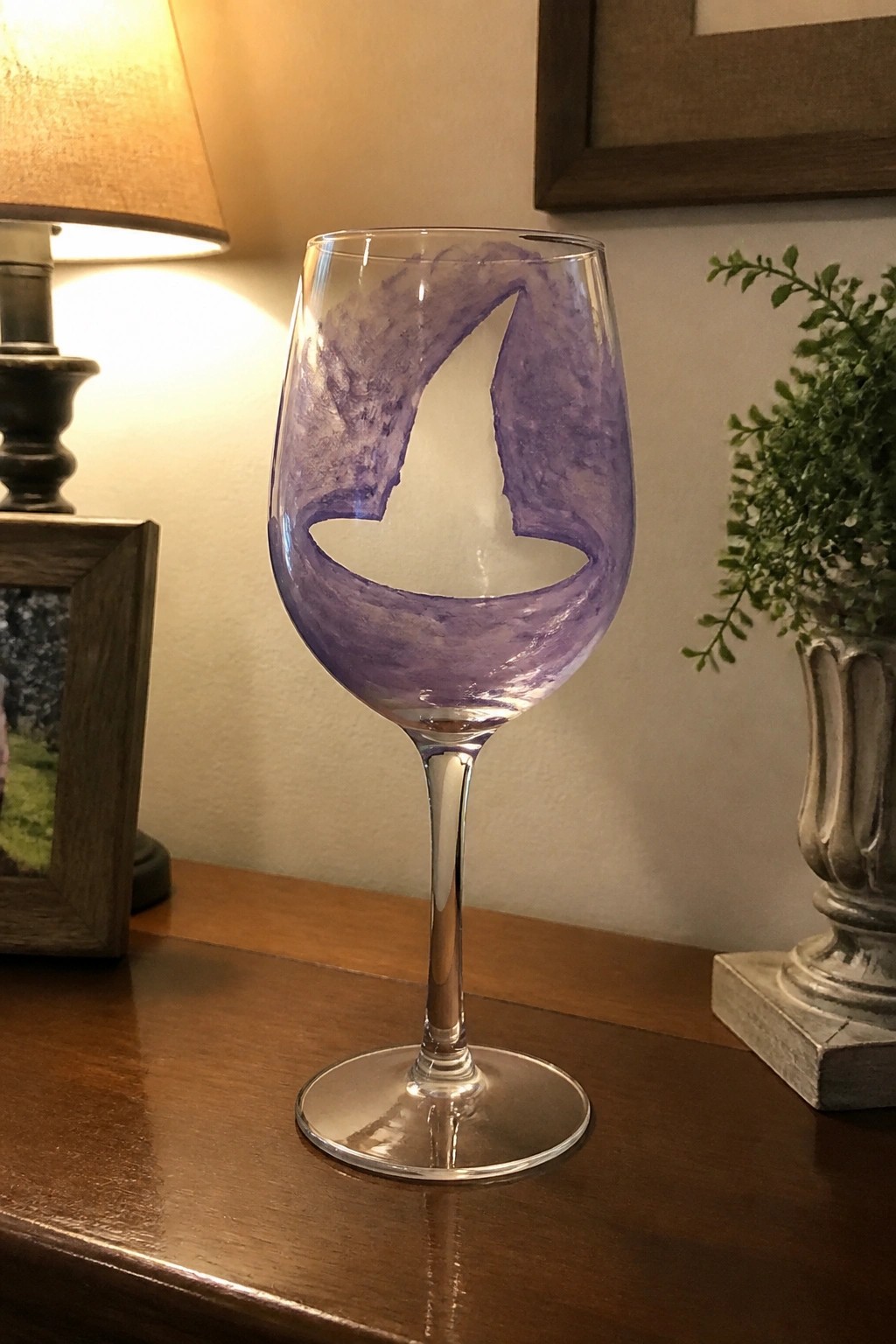 Wine glass with purple marbled sailboat design on wooden table with lamp and plant