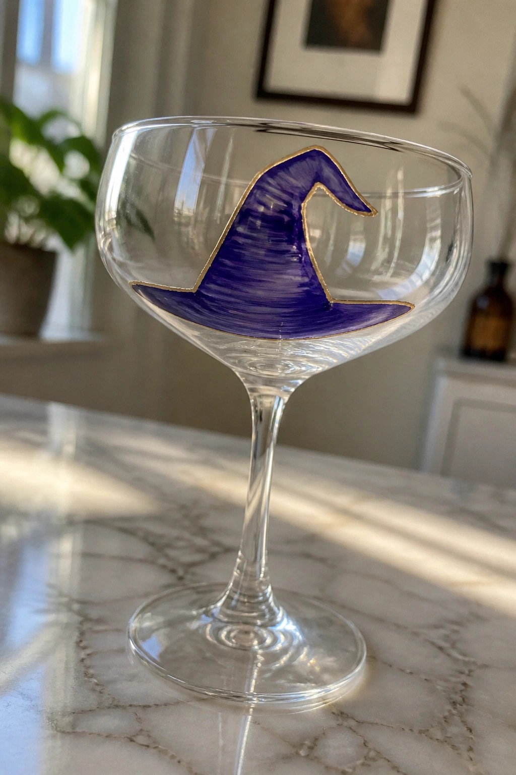 Clear coupe glass with purple witch hat and gold outline on marble.