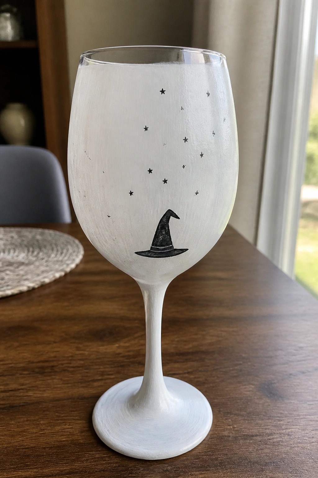 White painted wine glass with black witch hat and stars on wooden table