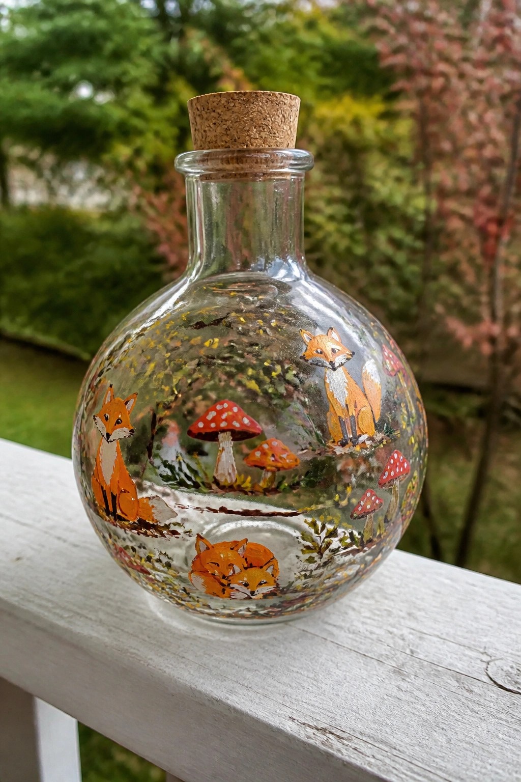 Glass bottle with cork, painted foxes and red mushrooms on white railing