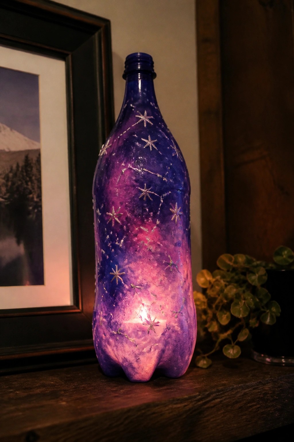 Glowing galaxy-painted plastic bottle with silver stars on wooden surface