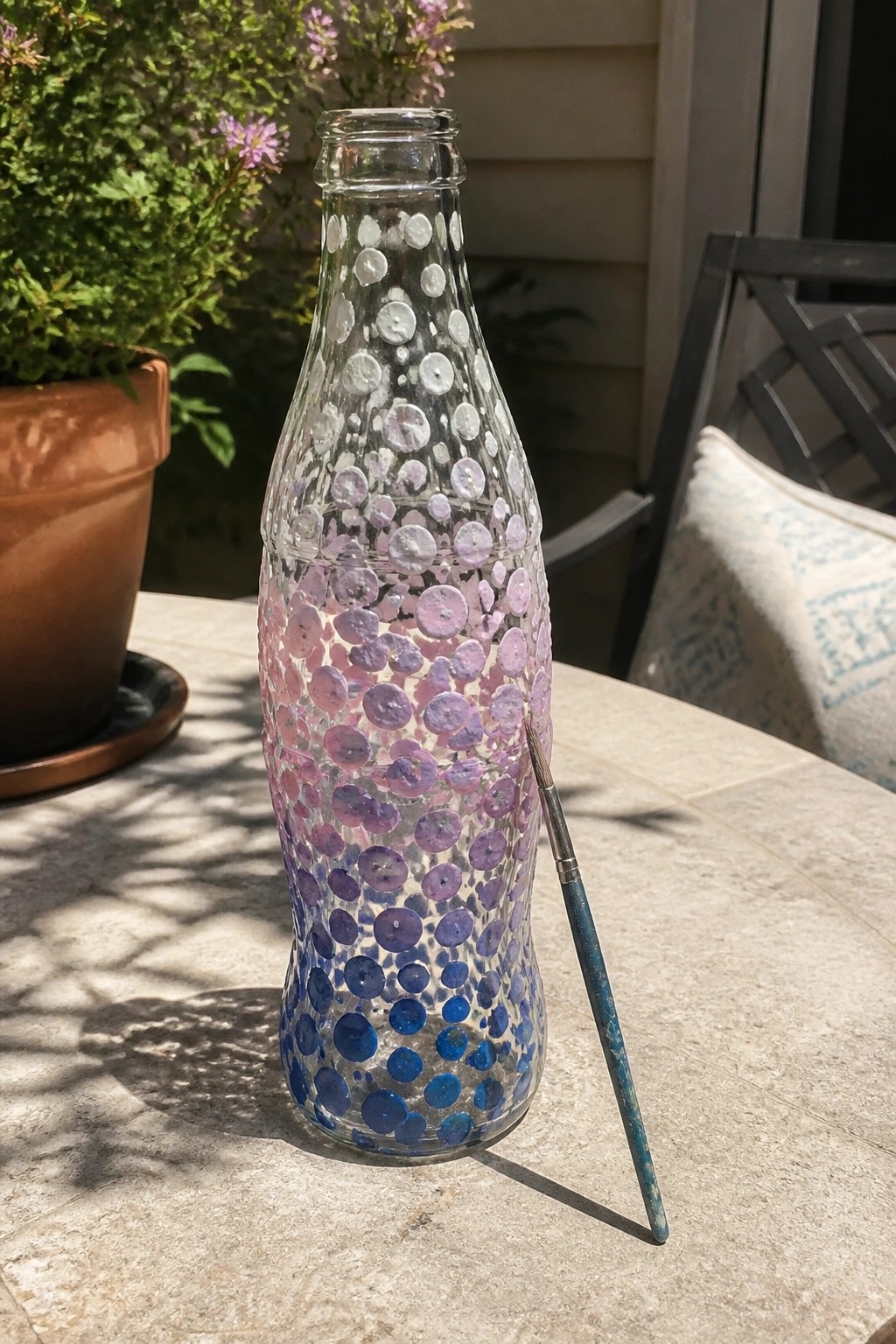 Glass bottle with purple-blue gradient dots beside paintbrush on outdoor table