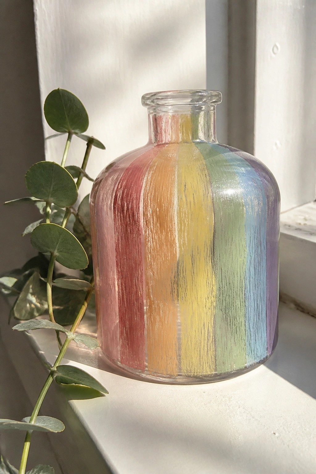 Rainbow-striped glass vase on sunny windowsill beside green eucalyptus plant