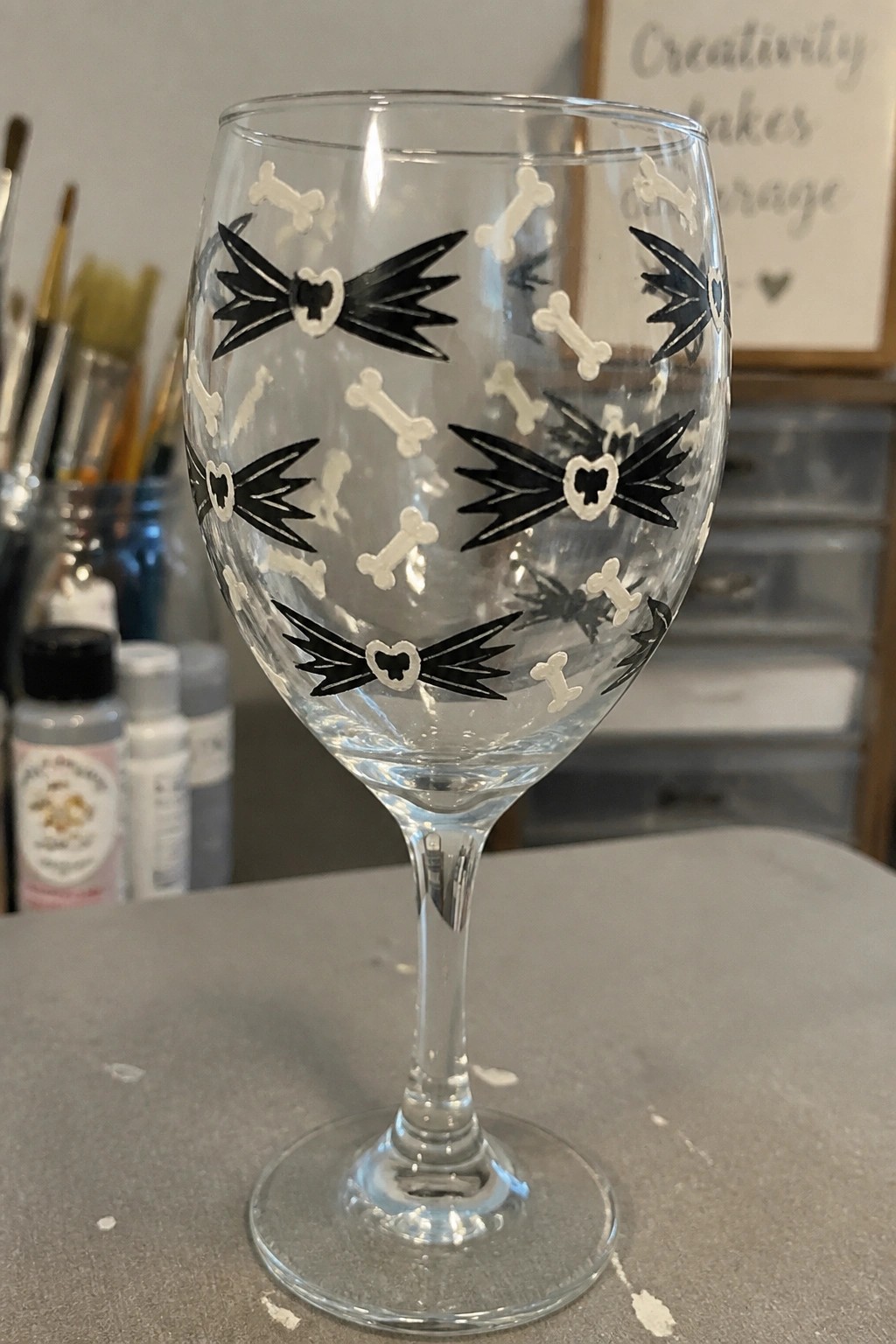 Clear stemmed wine glass painted with black winged bones, hearts, and white bones.