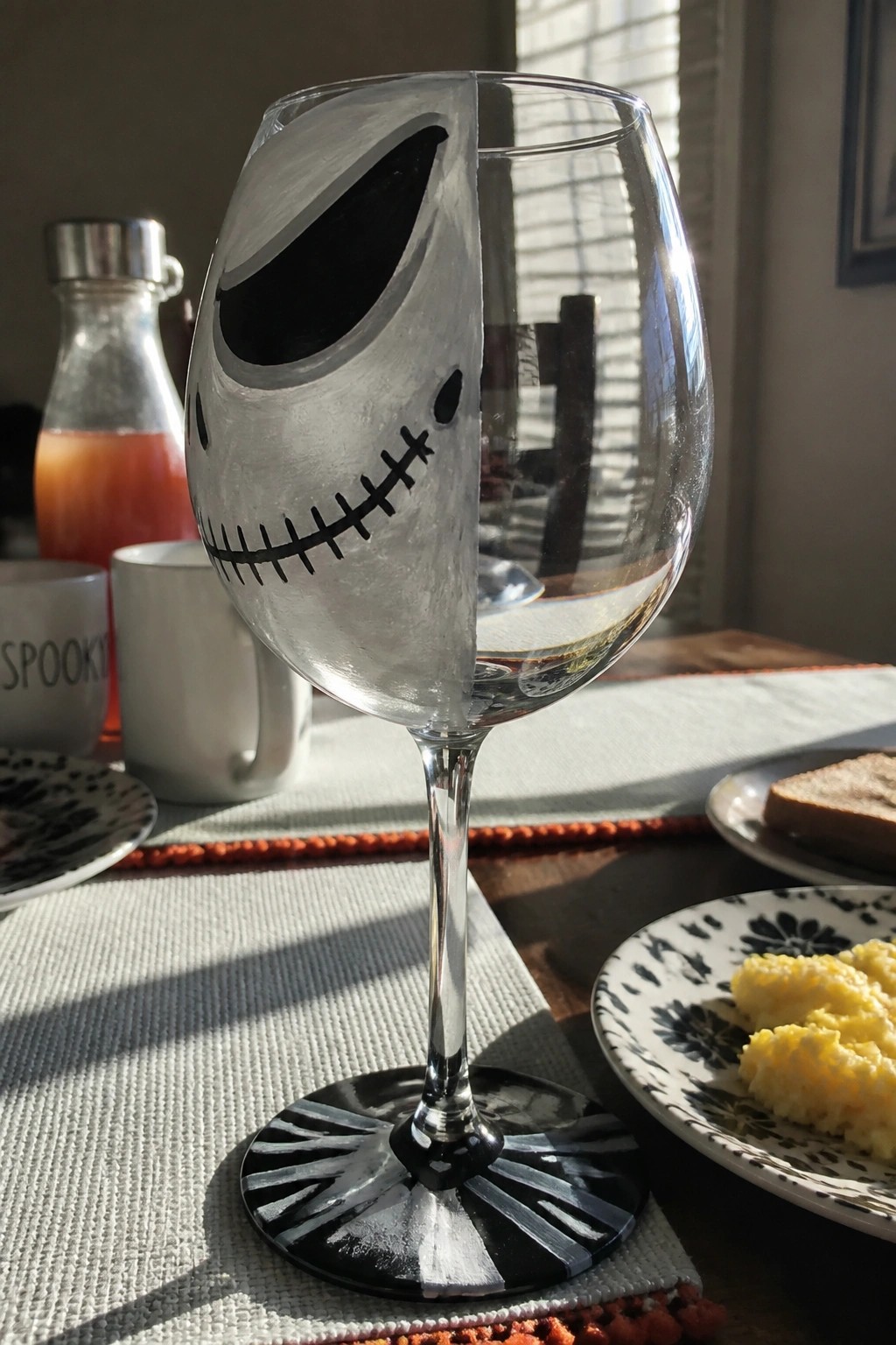 Hand-painted Jack Skellington wine glass on sunlit breakfast table with food.