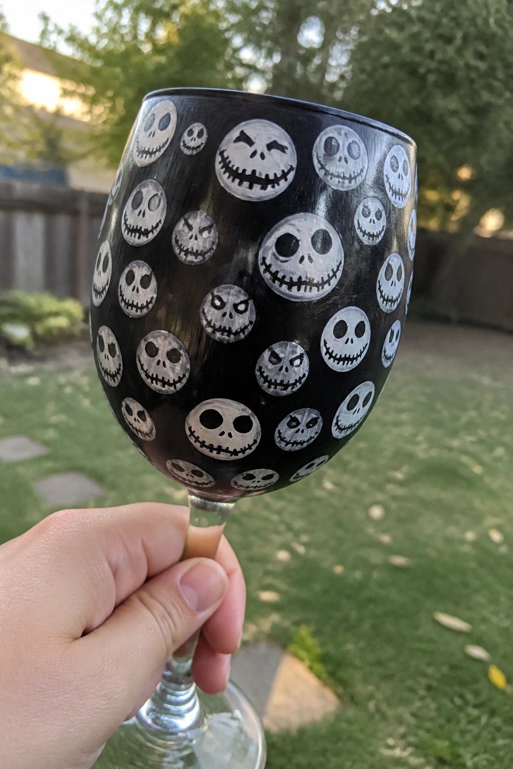 Hand holding black wine glass painted with assorted Jack Skellington faces outdoors