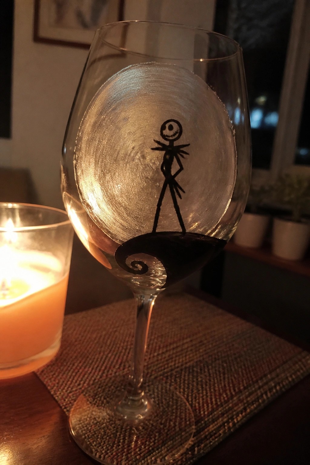 Wine glass painted with Jack Skellington beside lit candle on wooden table