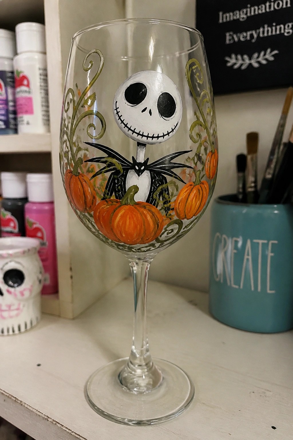 Hand-painted wine glass with Jack Skellington, orange pumpkins, and green vines.