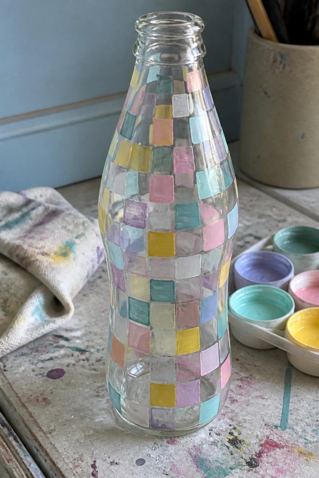 Glass bottle with pastel square paint patches on splattered art table