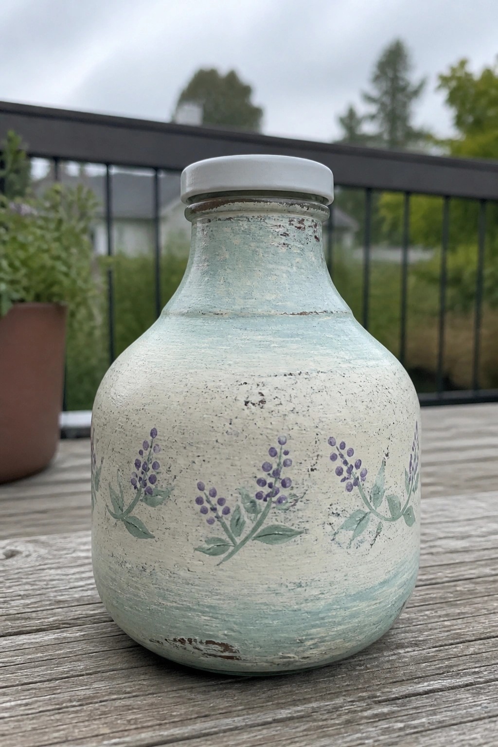 Distressed light blue glass bottle with purple floral designs and white lid on wood.
