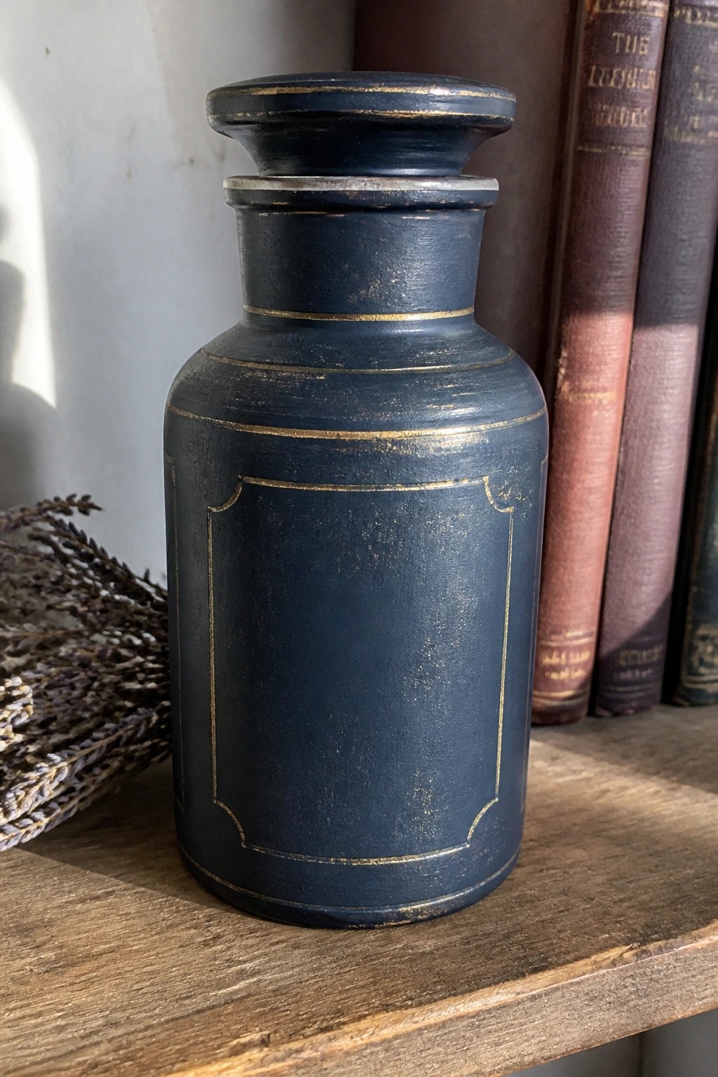Distressed dark blue vase with gold trim on wooden shelf near old books and lavender