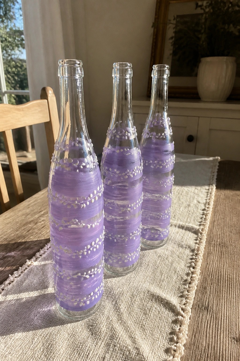 Three purple-striped glass bottles with white beads on burlap runner.