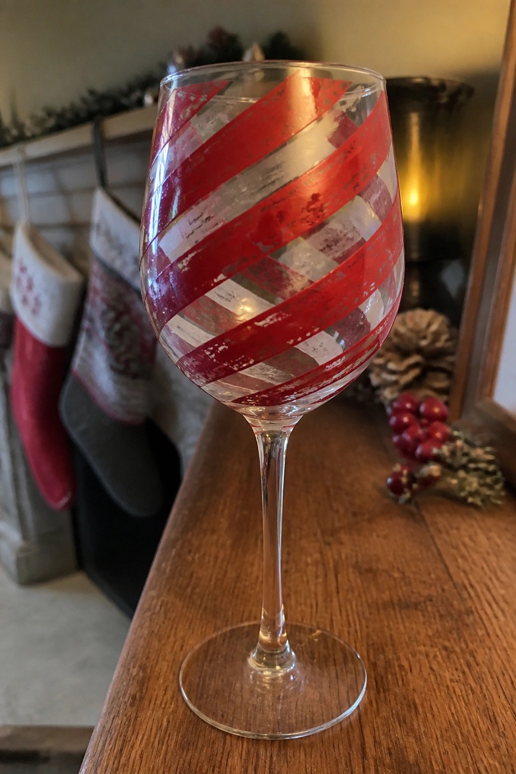Wine glass with red diagonal stripes on wooden table amid Christmas stockings and pinecones.