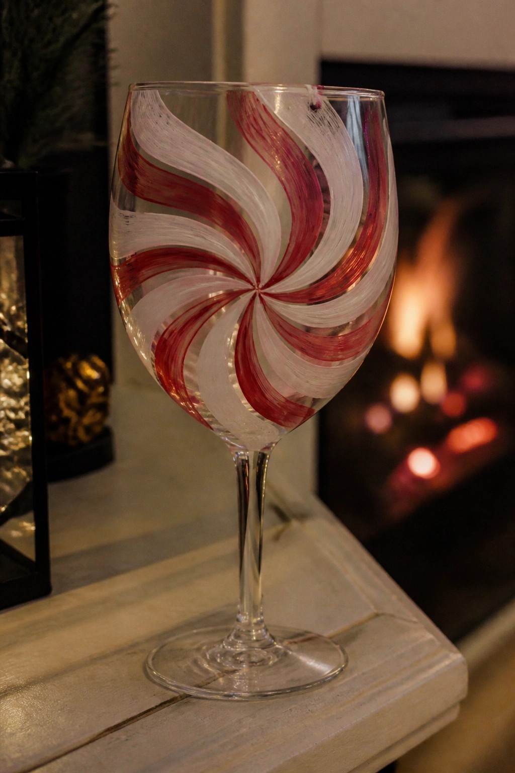Wine glass with red and white peppermint swirl design on wooden mantel near fireplace