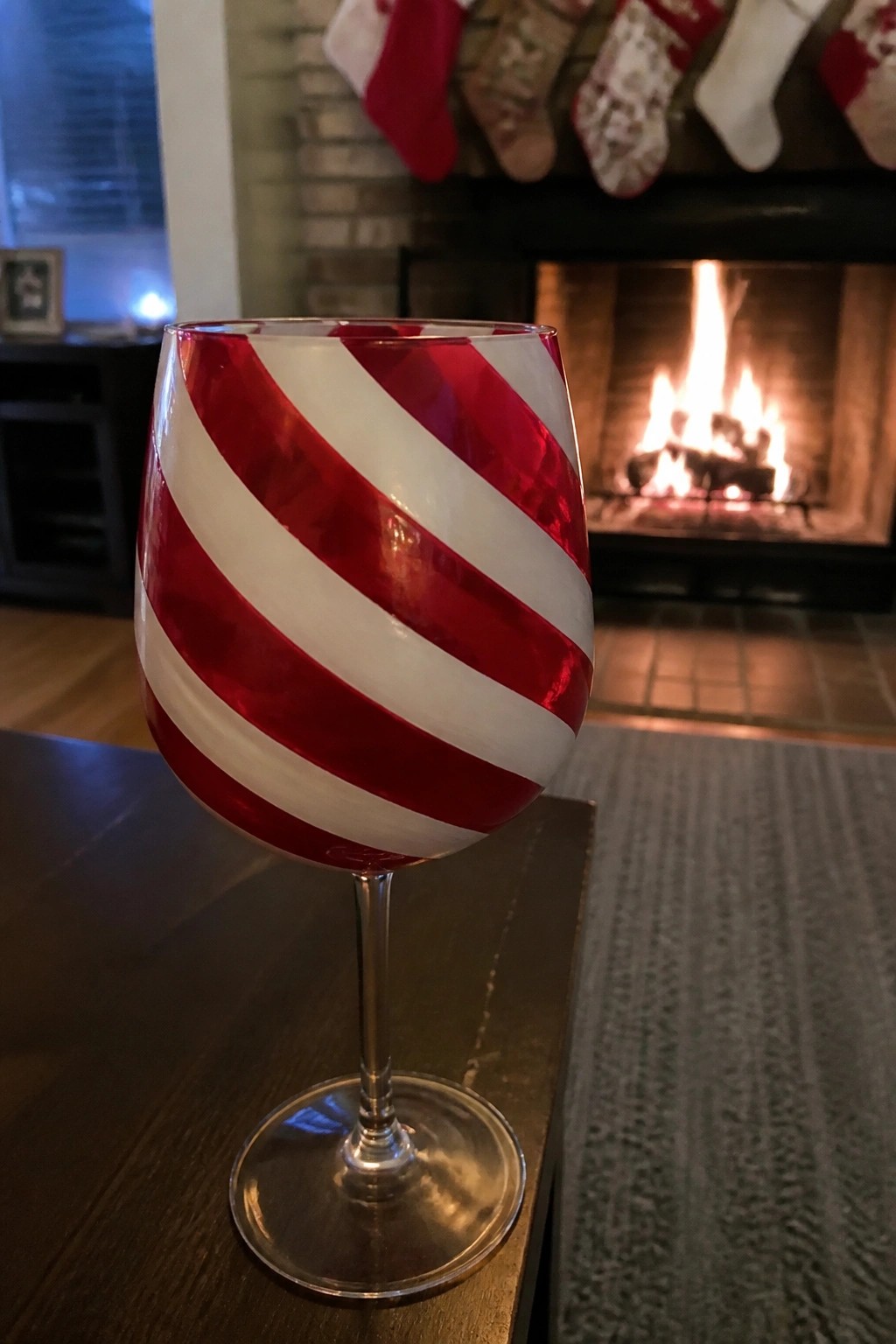 Red and white striped wine glass on table before lit fireplace with stockings