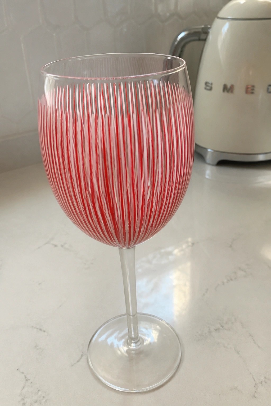 Wine glass with vertical red and white stripes on marble countertop near kettle