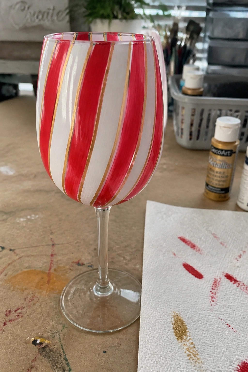 Red and white striped wine glass with gold lines on craft table.