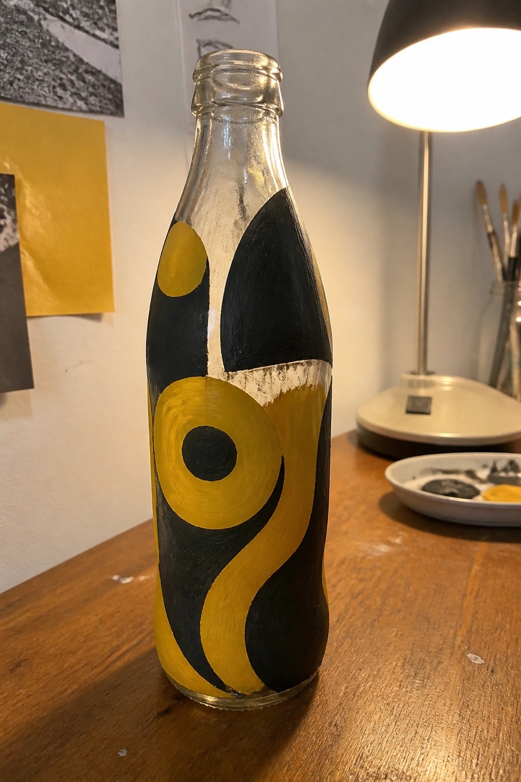 Glass bottle with bold yellow and black abstract painted designs on wooden table