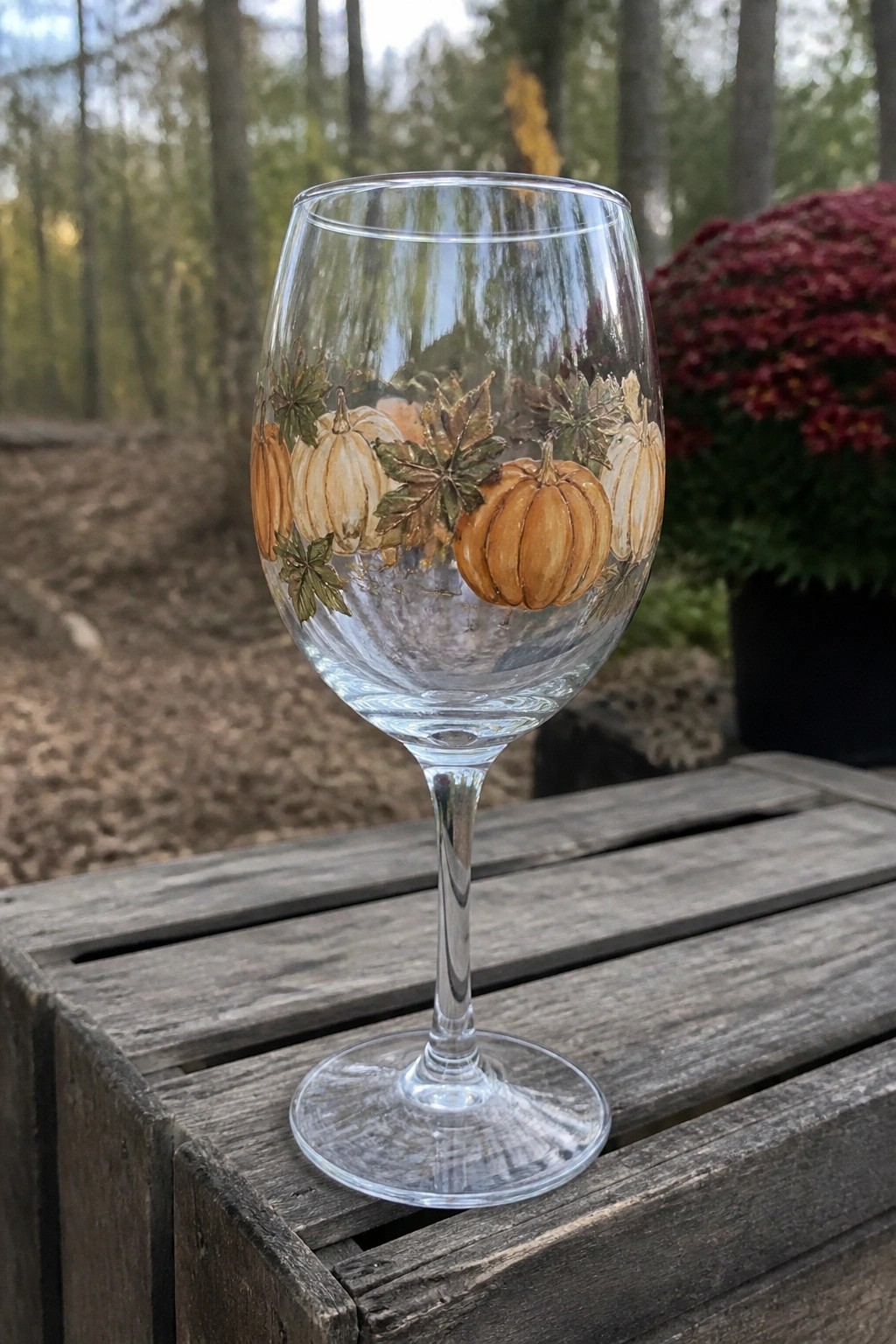Painted wine glass with orange pumpkins and autumn leaves on wooden table