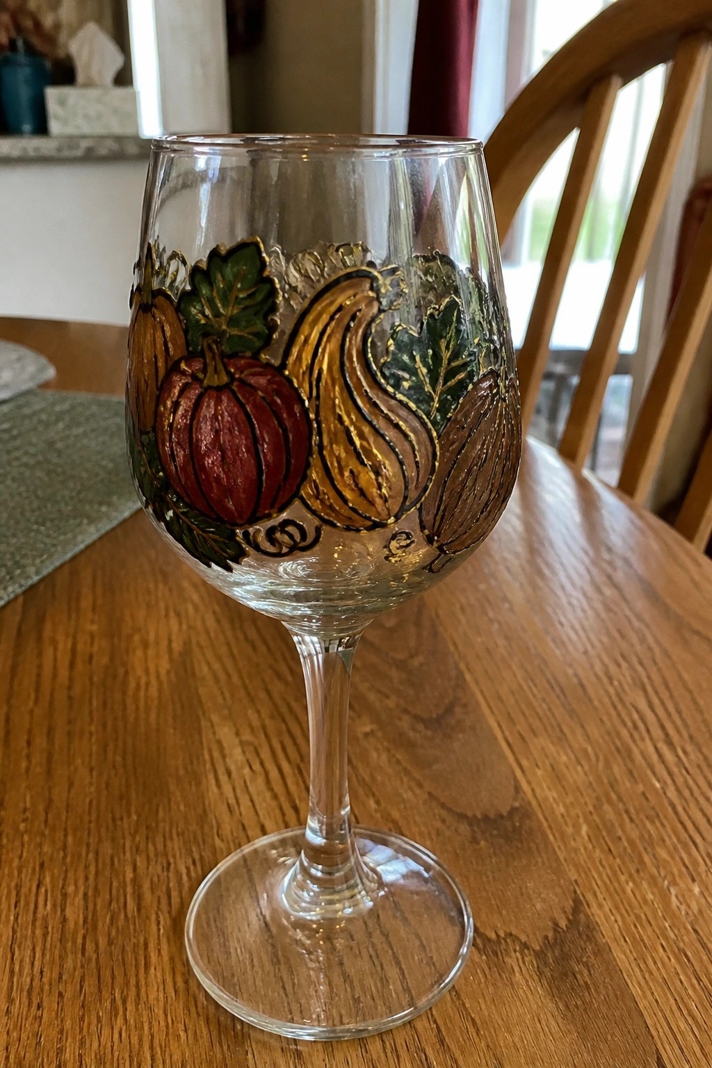 Clear wine glass hand-painted with red pumpkin, orange squash, and brown gourd.