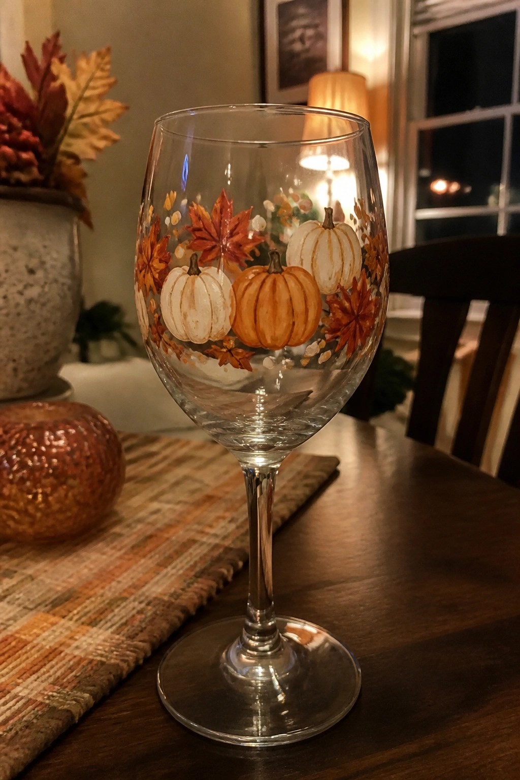 Wine glass hand-painted with white and orange pumpkins amid red maple leaves on table