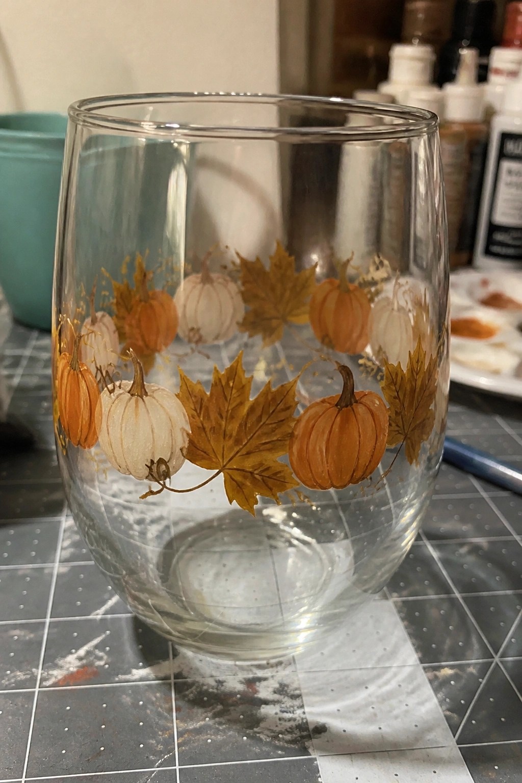 Clear glass tumbler hand-painted with orange pumpkins and yellow maple leaves on grid mat