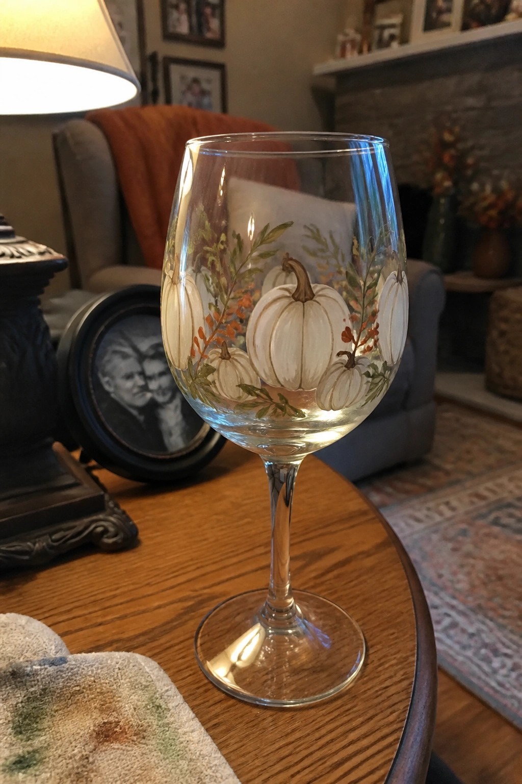 Wine glass hand-painted with white pumpkins, orange leaves, and green vines on wooden table