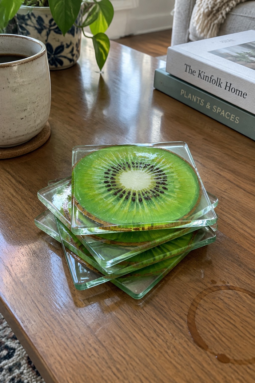 Stack of square kiwi slice coasters on wooden table with mug and books