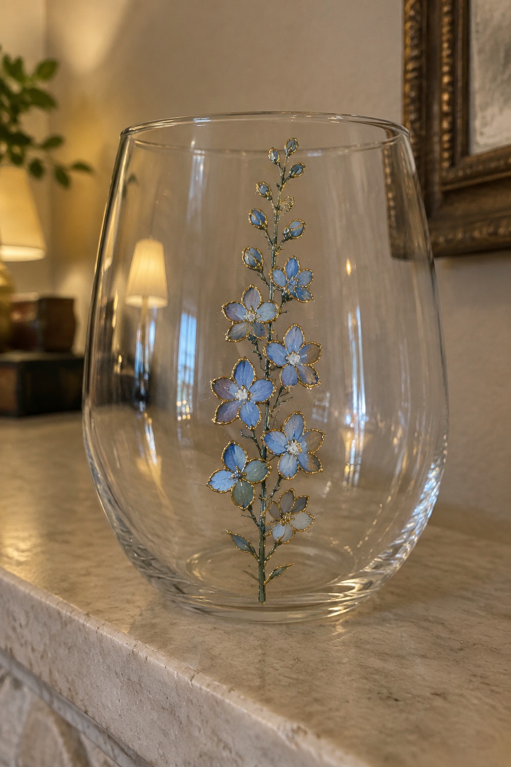 Clear glass tumbler with blue flowers and gold outlines on marble surface.
