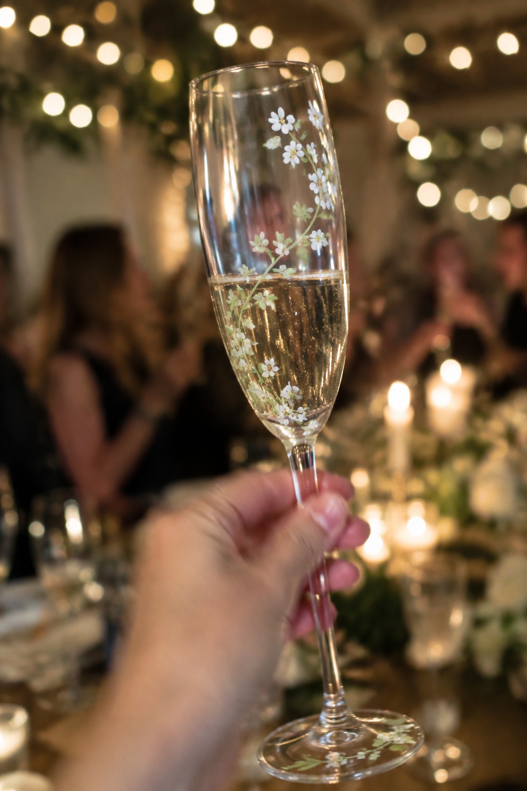 Hand holding floral-decorated champagne flute filled with sparkling wine at elegant event