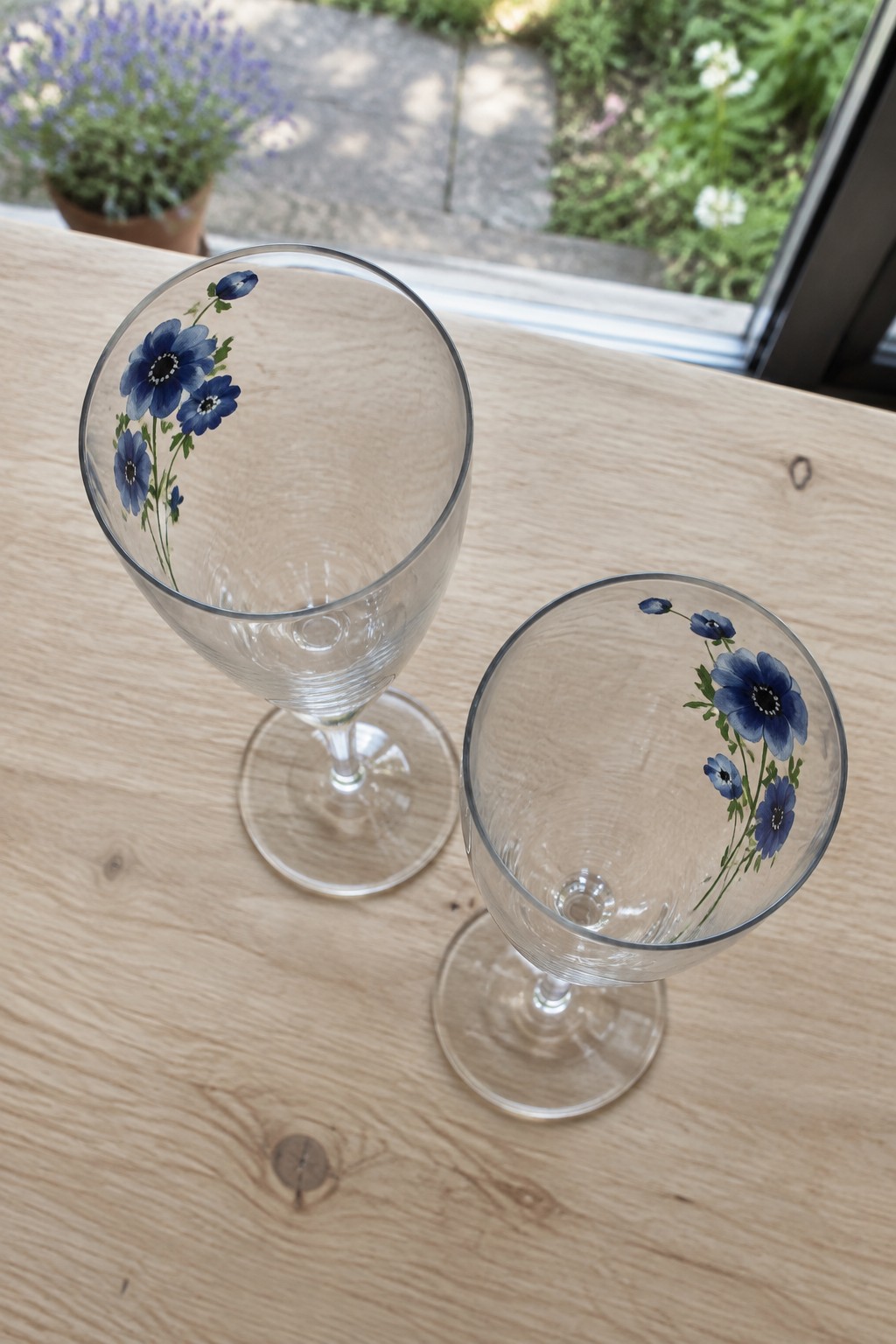 Two clear wine glasses with blue floral designs on a light wooden table.