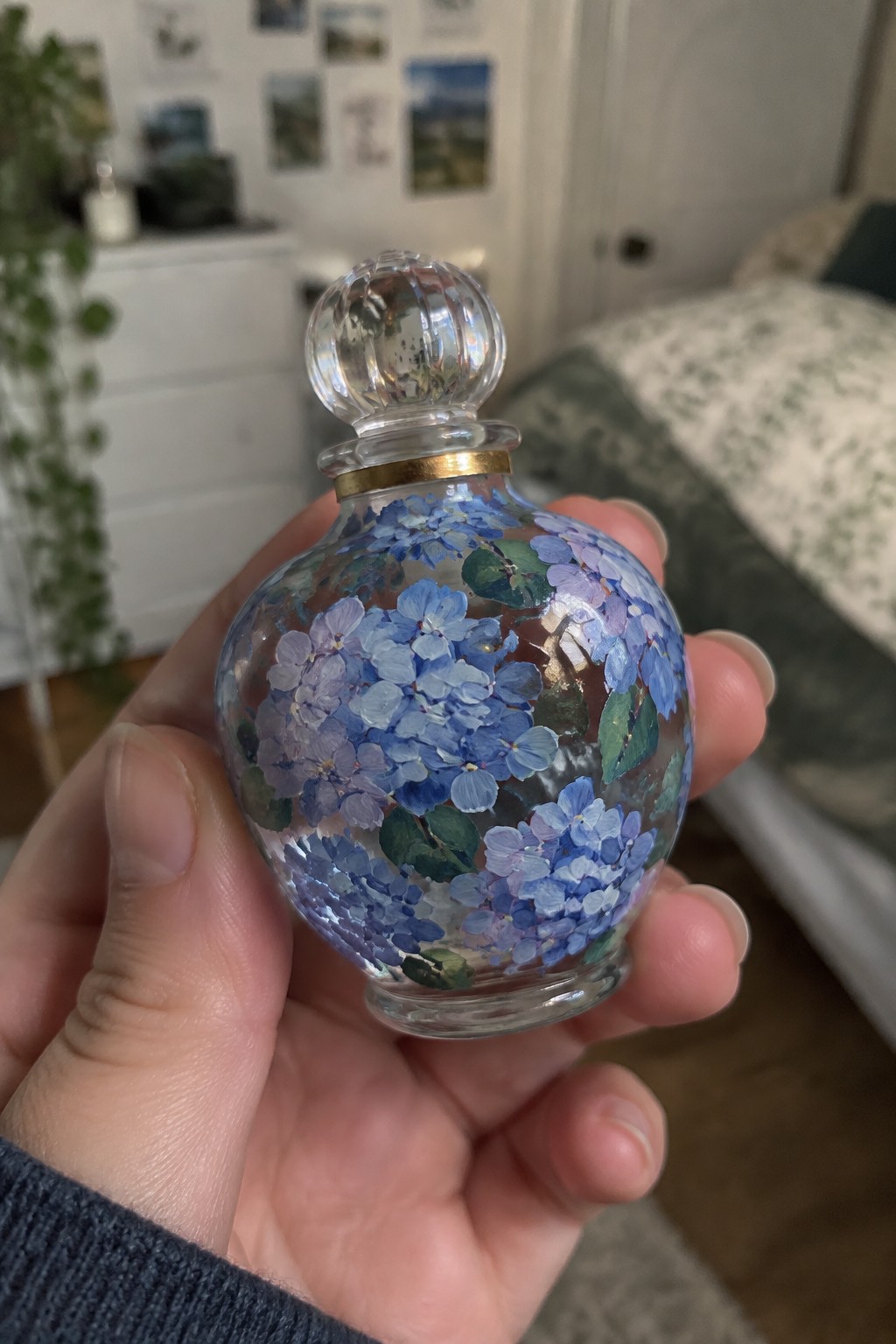 Hand holding round glass bottle painted with blue hydrangeas.