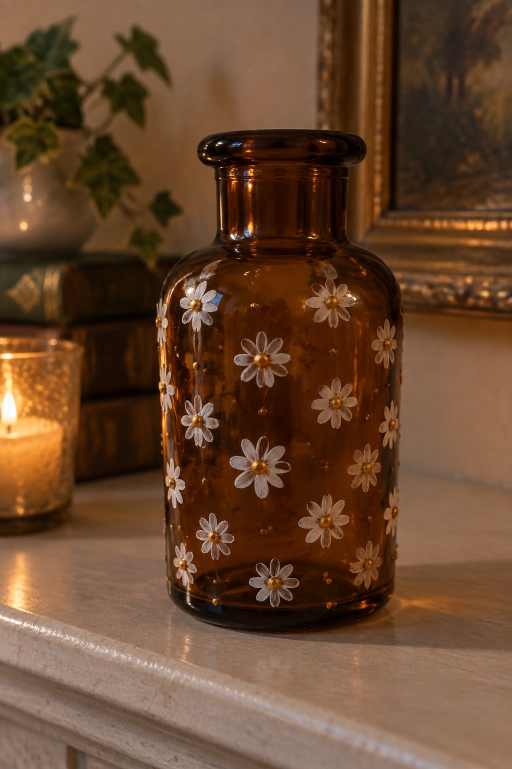 Amber glass vase with white daisies and gold dots beside a lit candle