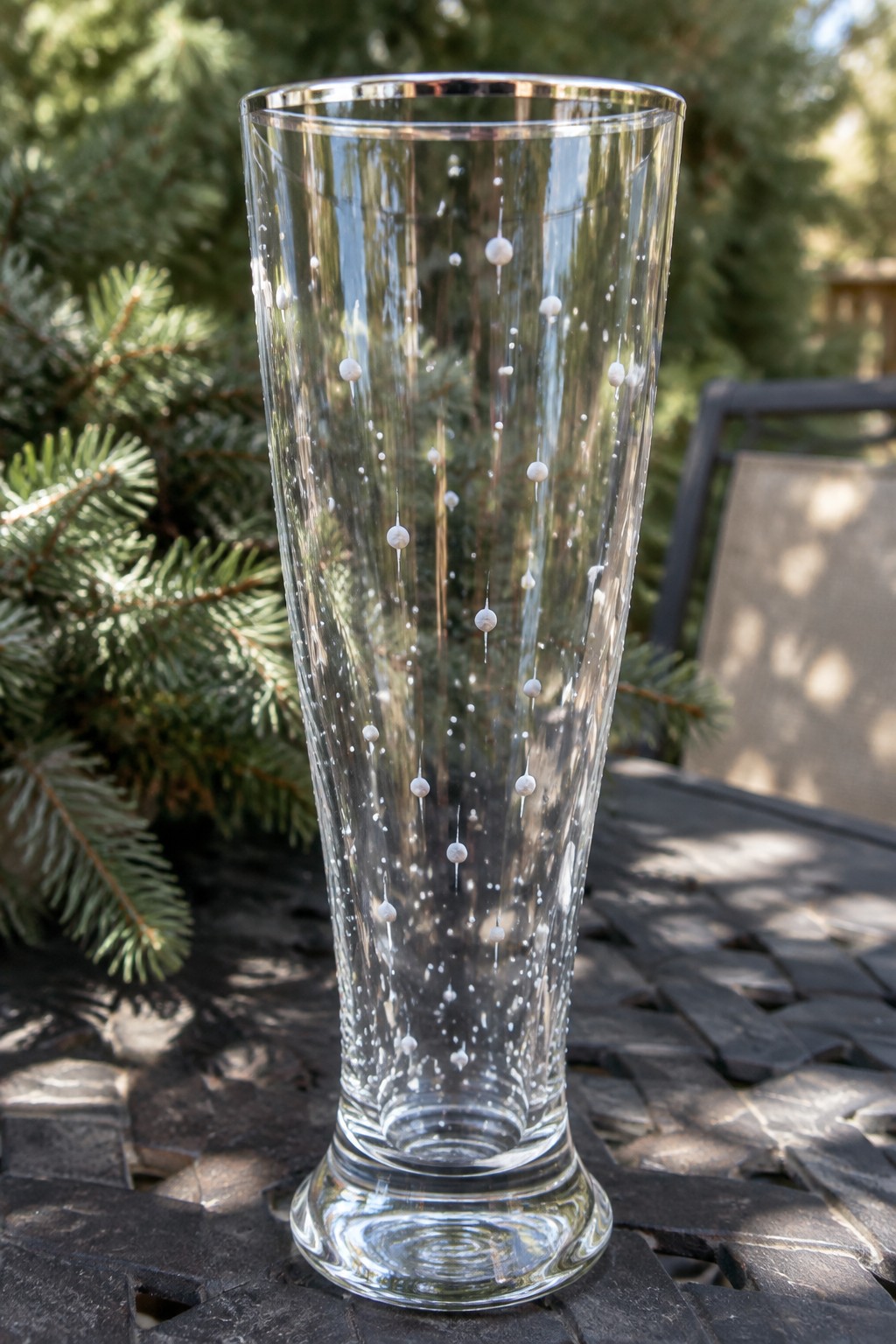 Tall clear glass vase with white bubble patterns on dark woven outdoor table