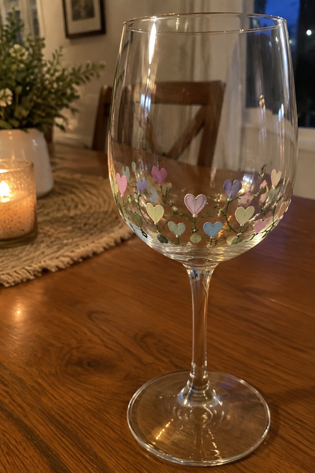 Clear wine glass painted with pastel hearts and green vines on wooden table