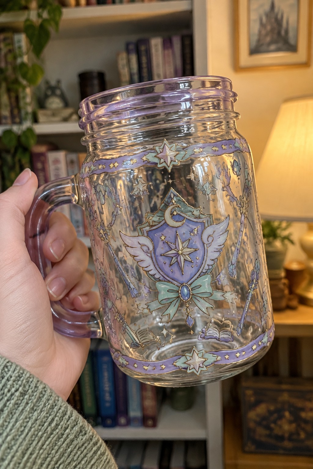 Hand holding ornate glass mug with purple shield, stars, wands, and bow.