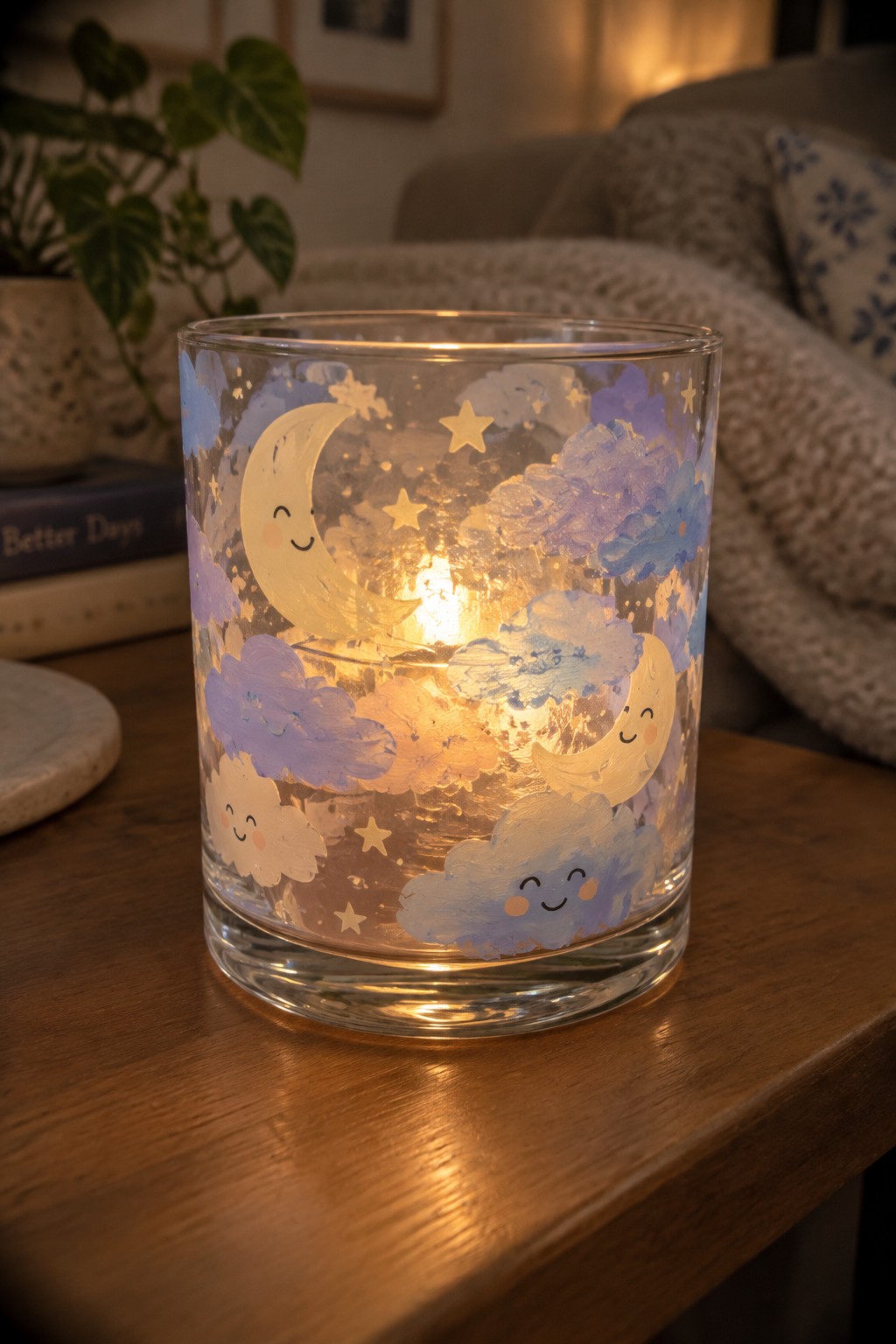 Lit candle in glass jar painted with smiling moons, clouds and stars