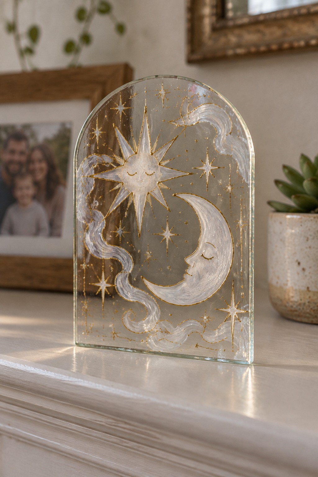Arched glass panel with sun, moon, stars, and gold swirls on white surface.
