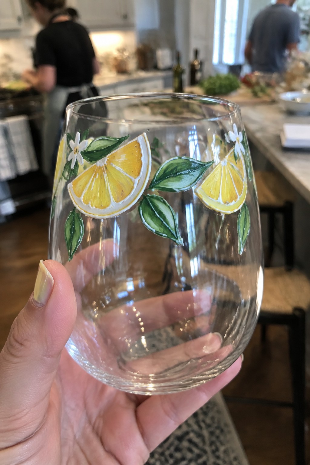 Hand holding clear stemless glass painted with yellow lemons, green leaves, and white flowers