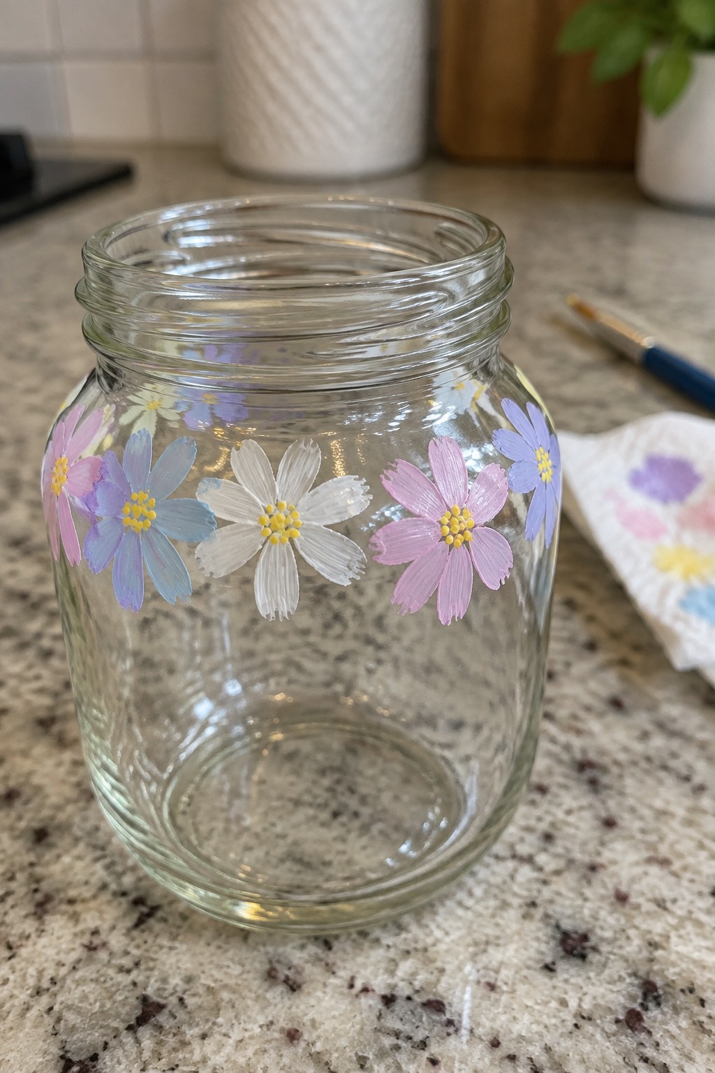 Glass jar with pink purple blue white painted flowers on marble counter