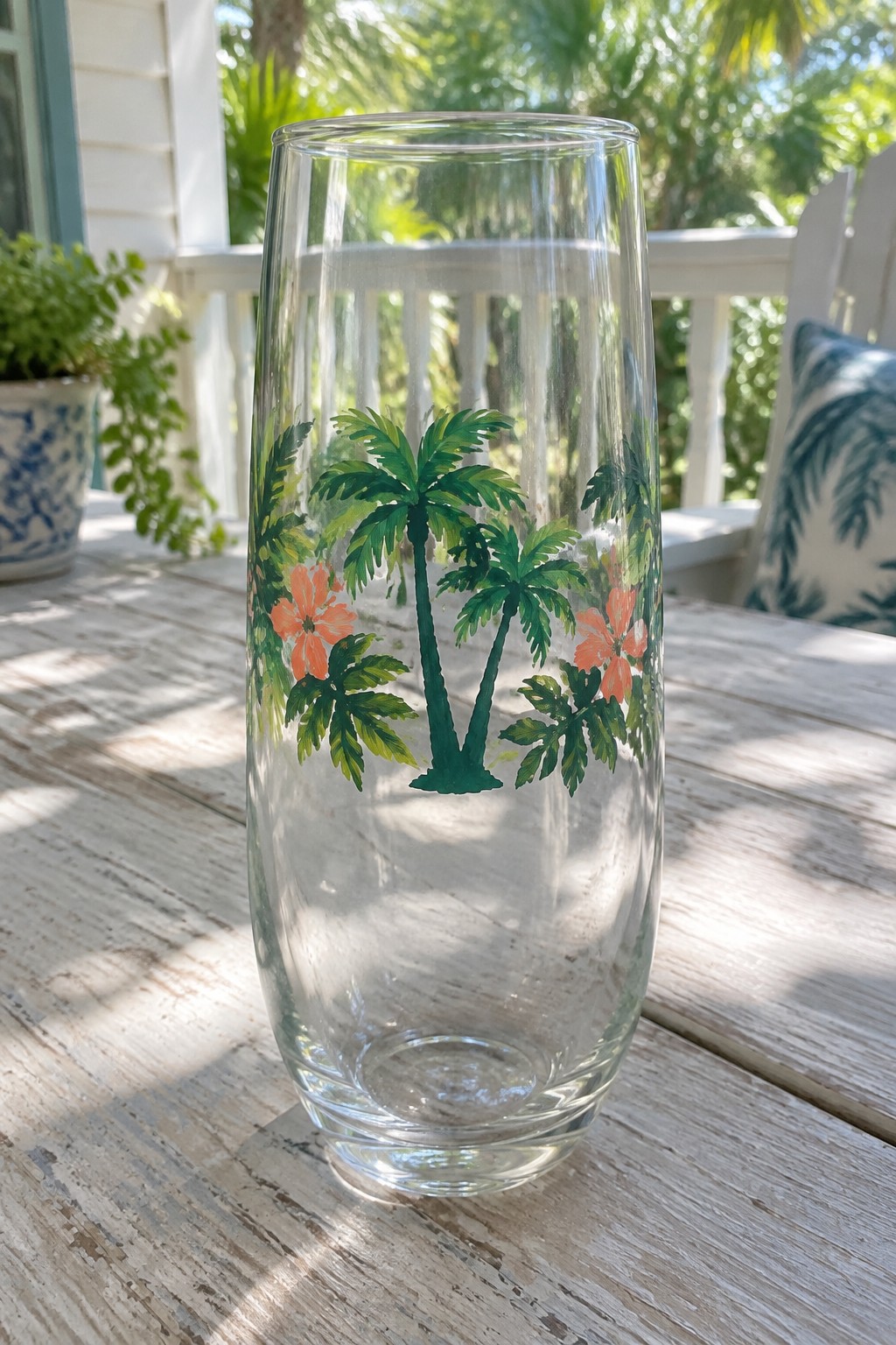Clear glass tumbler with green palm trees and orange flowers on wooden table