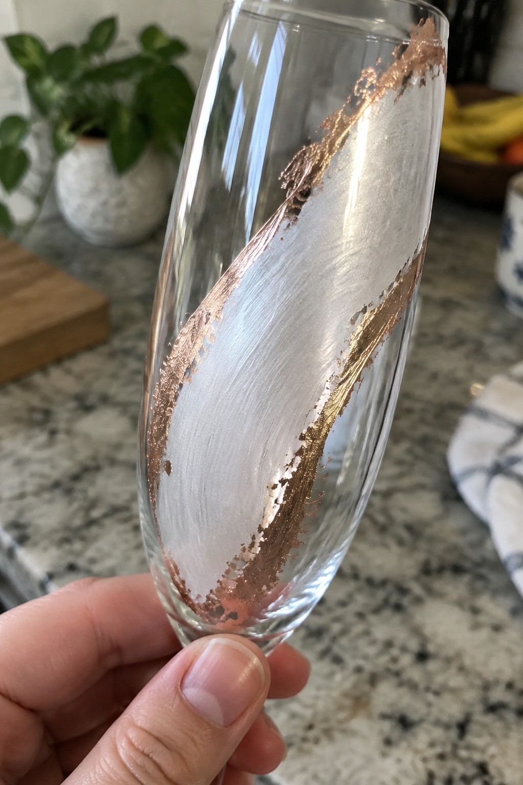 A hand holding a clear champagne flute with a wide diagonal metallic copper painted stripe.