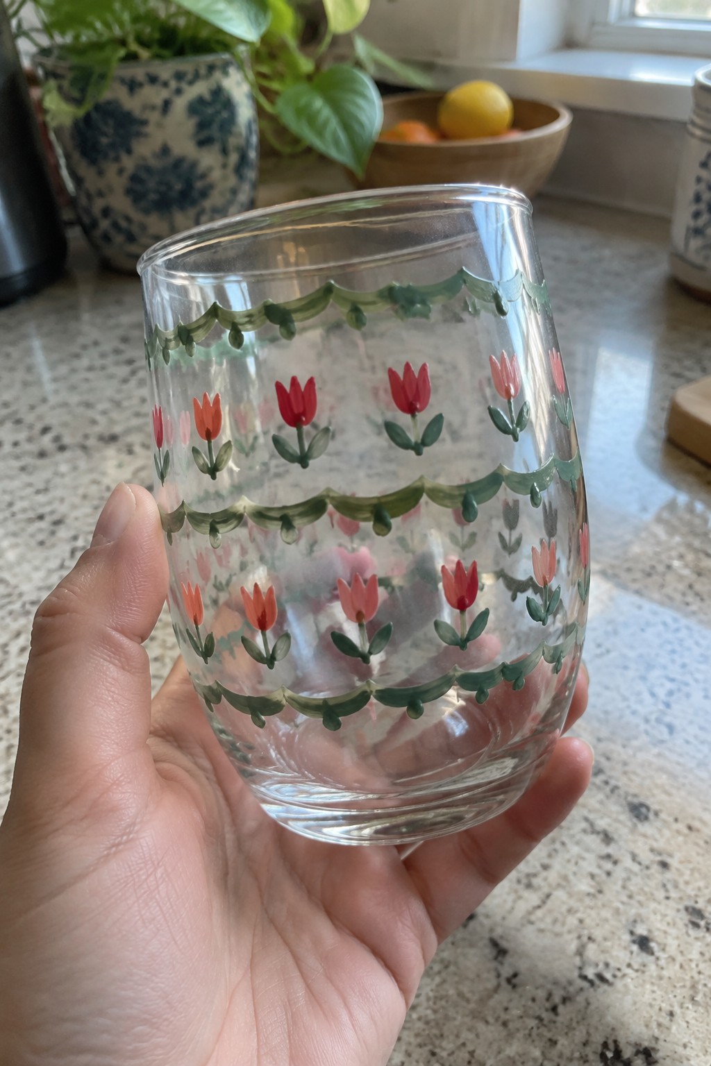 Hand holding clear glass tumbler with green scallops and red-pink tulips