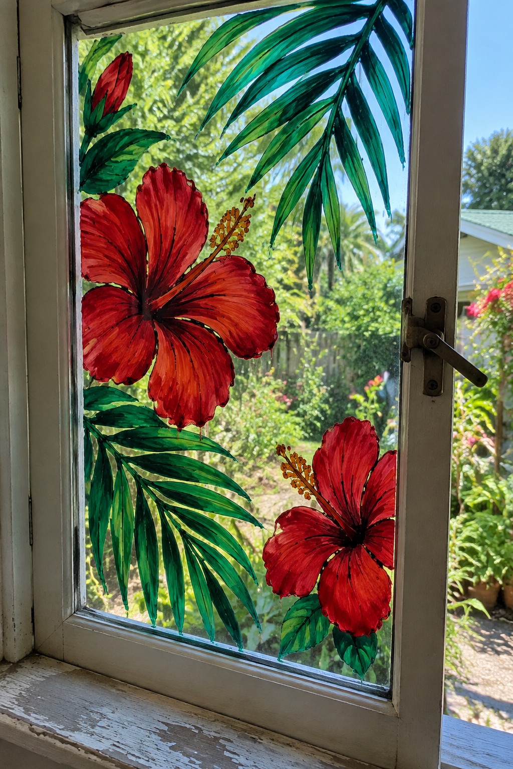 White window with red hibiscus flowers and green leaves painted on glass, garden beyond