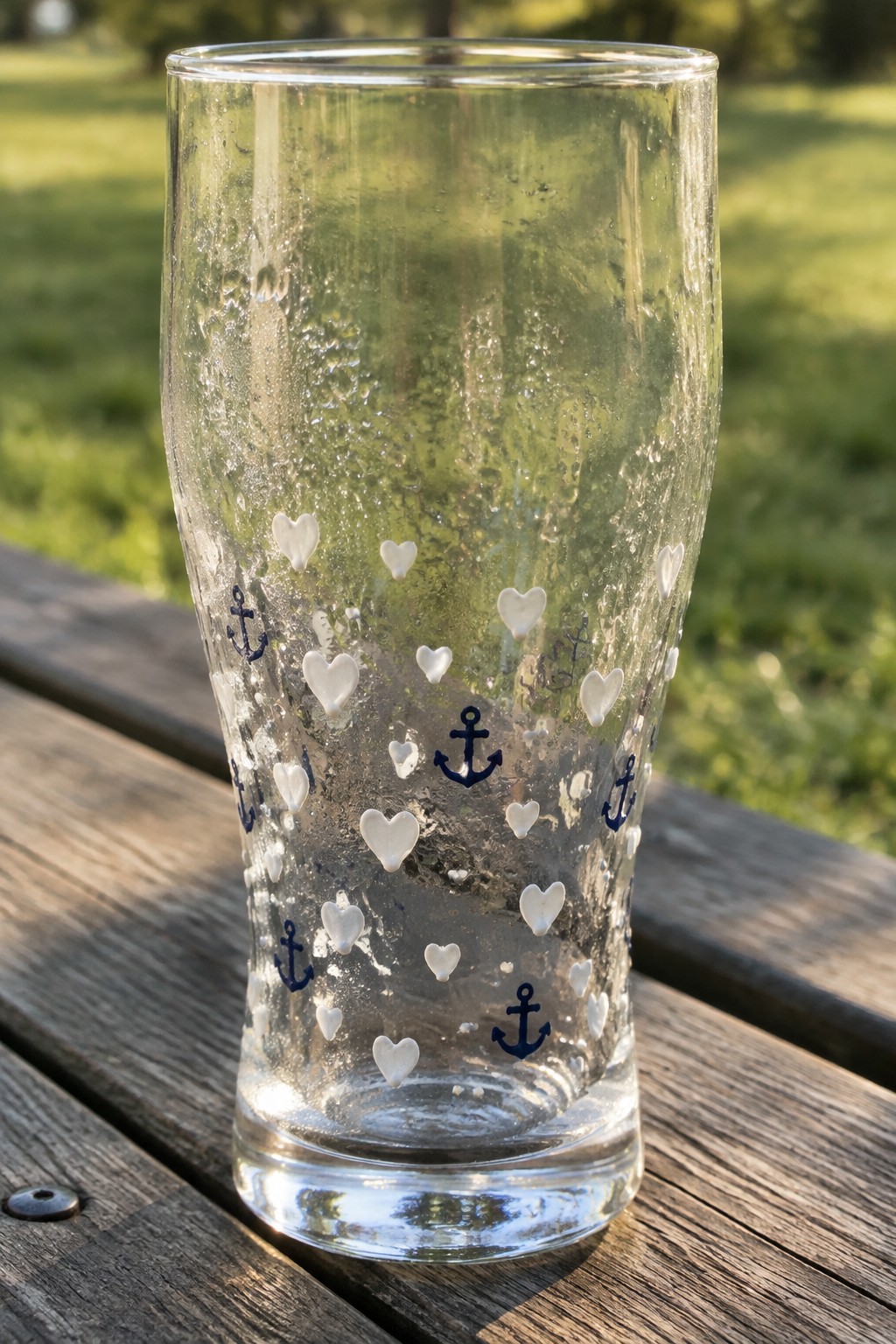 Clear glass with condensation, white hearts and blue anchors on wooden table