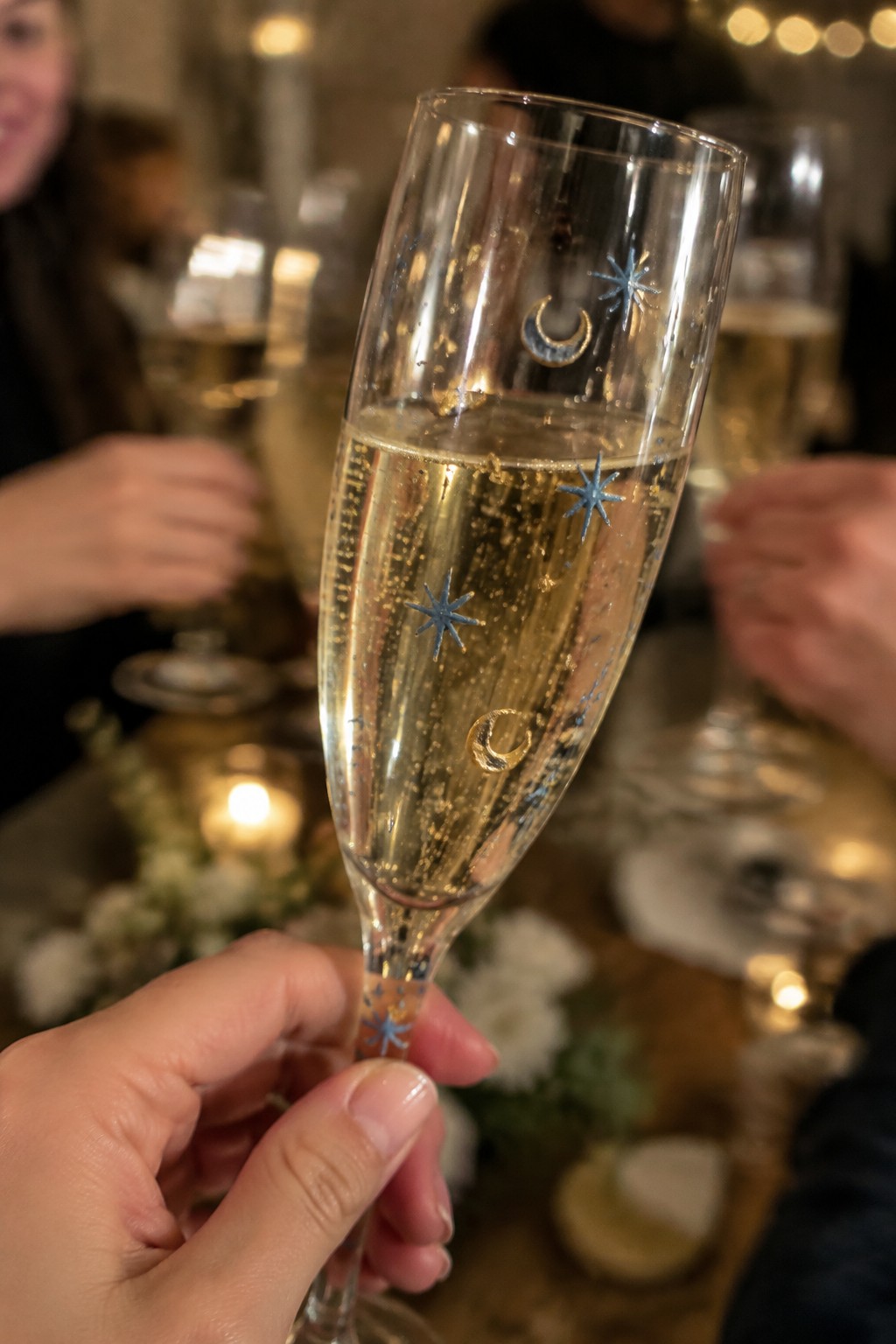Hand holding champagne flute with blue stars and gold crescent moons at festive table