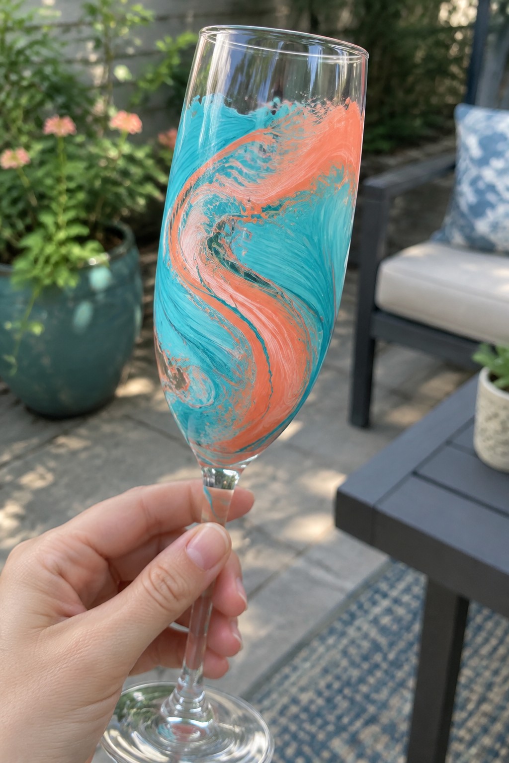 Hand holding marbled turquoise and coral champagne flute on outdoor patio