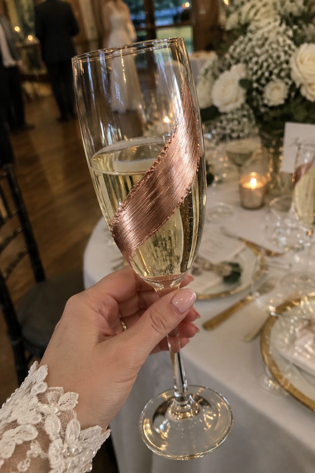 Hand in white lace holding rose gold champagne flute at elegant wedding table