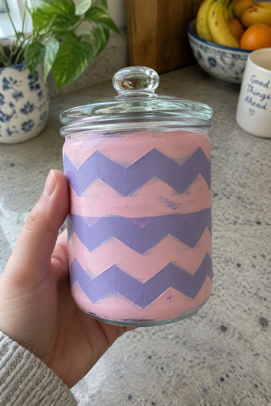 Hand holding pink jar with purple chevron pattern and glass lid on counter